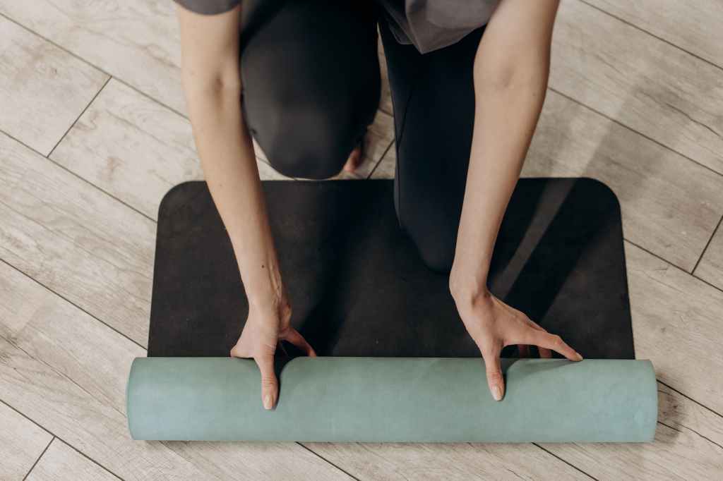 Woman kneeling and unrolling black yoga mat.